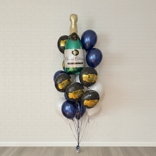 Bouquet of balloons shaped like a bottle of champagne against a white brick wall.
